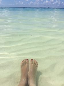 Person dipping feet in turquoise ocean waters, symbolizing grounding and connection with nature