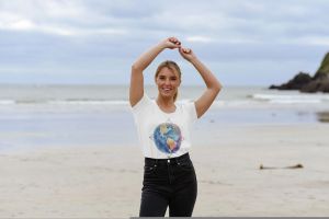 Woman wearing a Gaia's Threads T-shirt featuring a watercolor illustration of the Earth intertwined with the Flower of Life symbol.