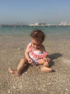 Baby playing in the sand with the ocean in the background, illustrating the mindfulness of kids at play