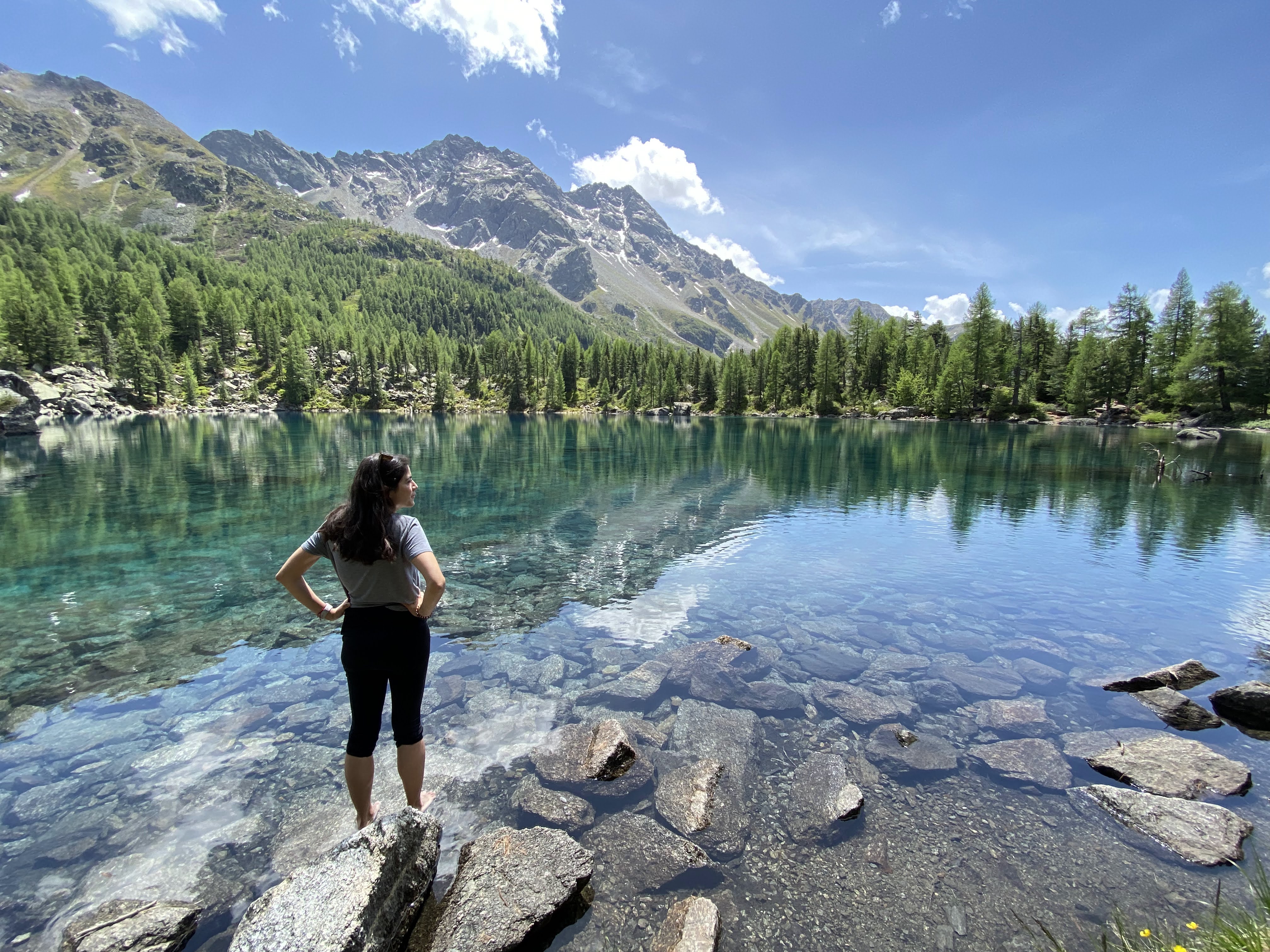 A person dipping their toes in the clear waters of Lago di Saoseo in Switzerland, emphasizing the benefits of grounding practices for health and connection with the Earth.