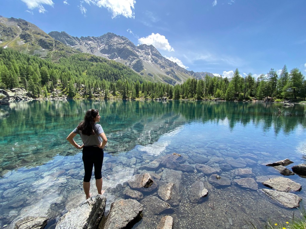 A person dipping their toes in the clear waters of Lago di Saoseo in Switzerland, emphasizing the benefits of grounding practices for health and connection with the Earth.
